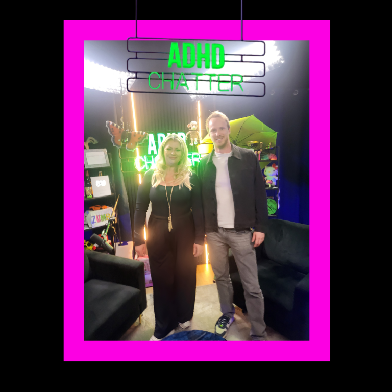 Two people stand together in a brightly coloured studio with neon signs.